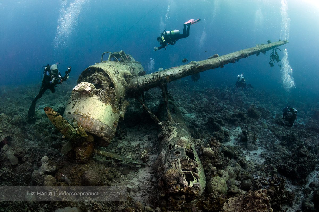 Underwater photograph of the WWII Jake seaplane wreck, with male and female scuba divers photographing it. Jake seaplane was a 3 seat, single engine and twin float seaplane.